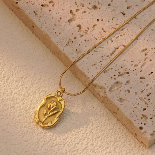 Gold necklace with a pendant on a textured beige surface