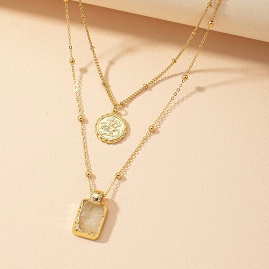 Gold necklace with two pendants on a beige background