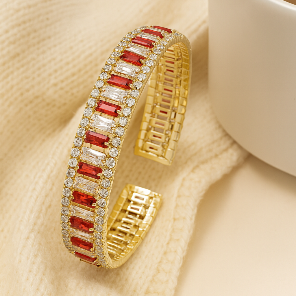 Gold bangles with red stones on a beige fabric background with a cup of coffee.