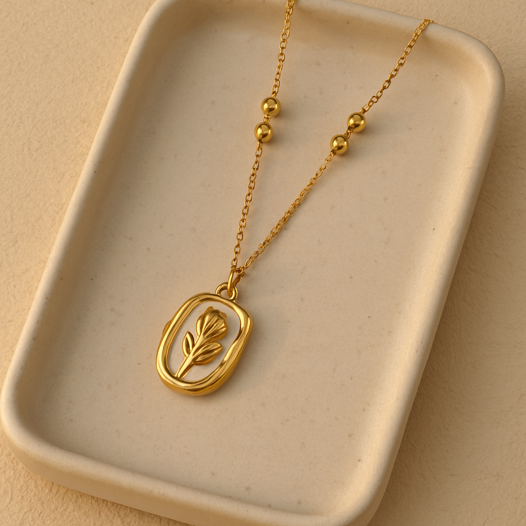 Gold necklace with a leaf pendant on a beige tray