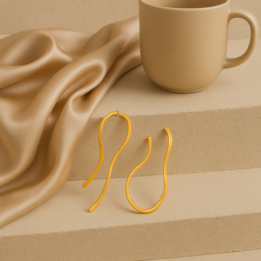 Gold earrings on a beige fabric with a matching mug