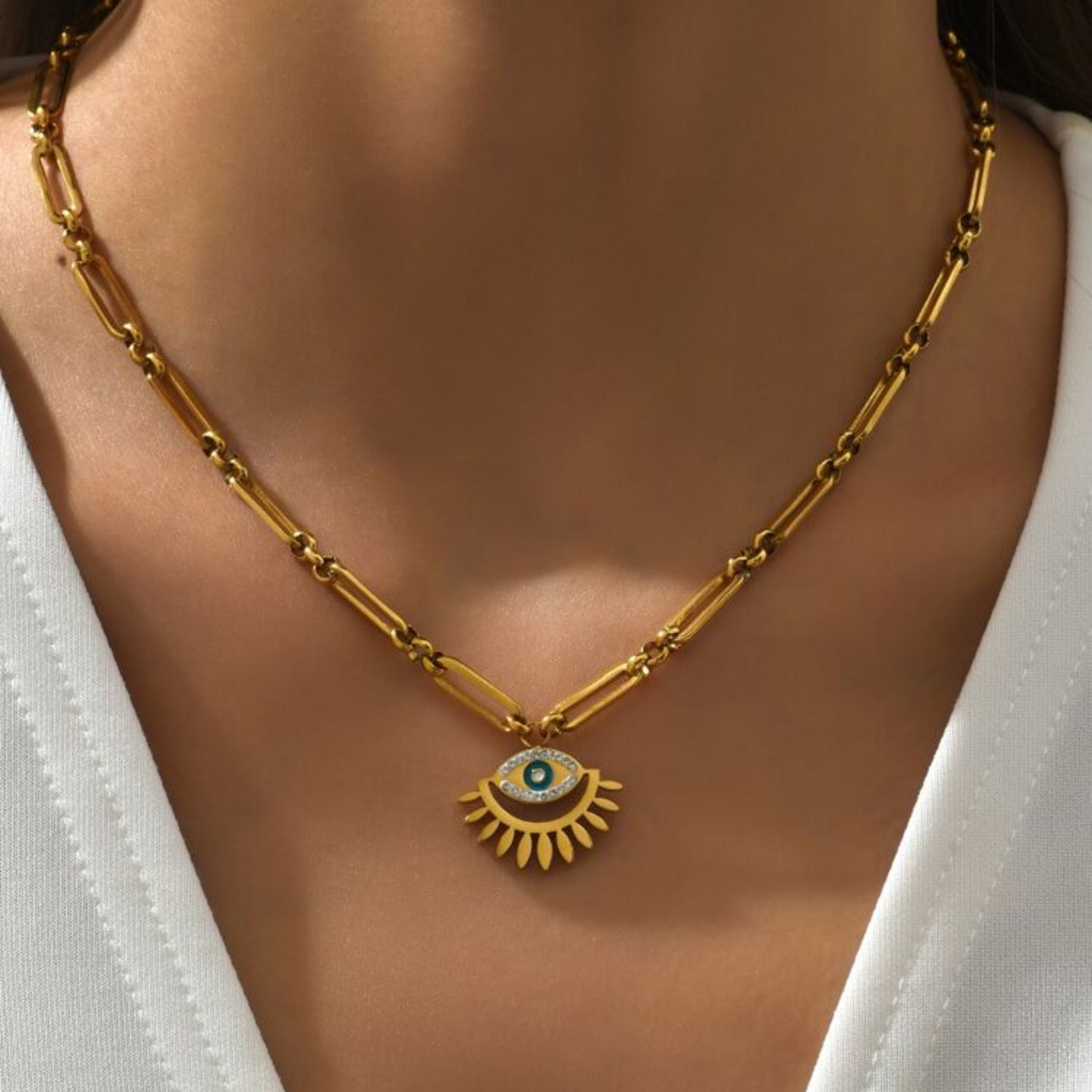 Gold necklace with an eye pendant worn by a person in a white top