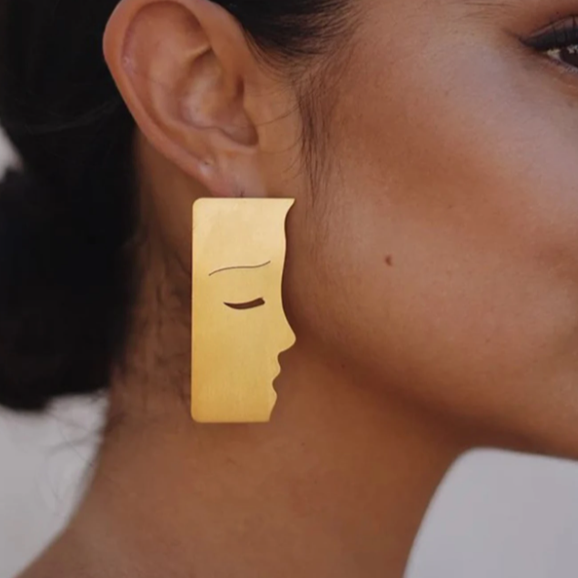 Gold earring with face design worn by a person