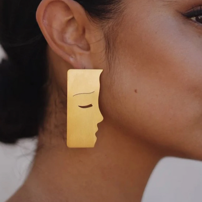 Gold earring with face design worn by a person