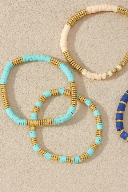 Three beaded bracelets in turquoise, gold, and blue on a beige background