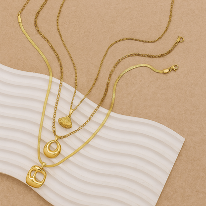 Three gold necklaces with various pendants on a beige background