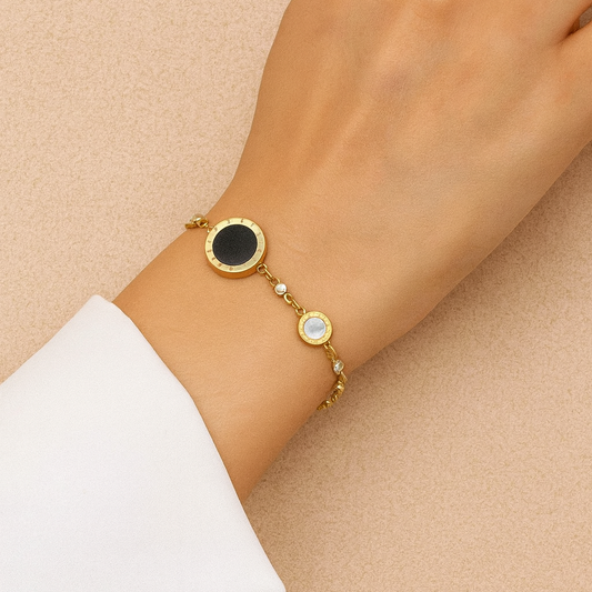 Gold bracelet with black and white gemstones on a wrist against a beige background