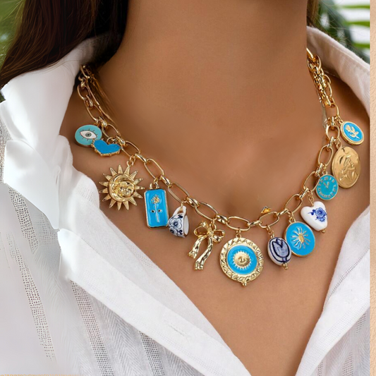 A person wearing a white shirt showcasing a gold-toned necklace with multiple charms including a bow, heart, sun, coin, and textured metal pendants.