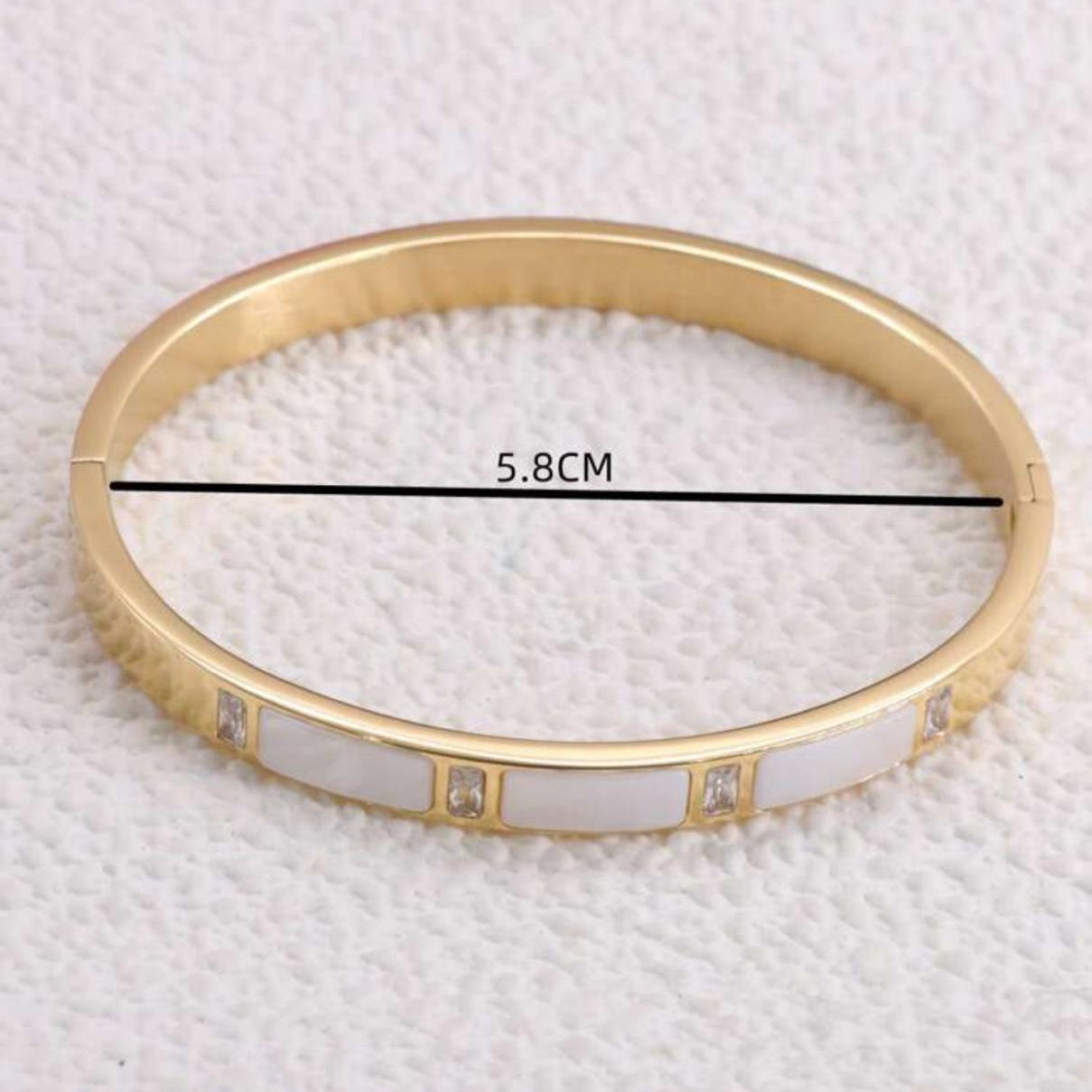Gold bracelet with white stones on a textured white background