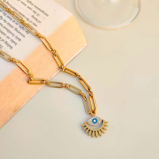 Gold necklace with a pendant on an open book next to a glass.